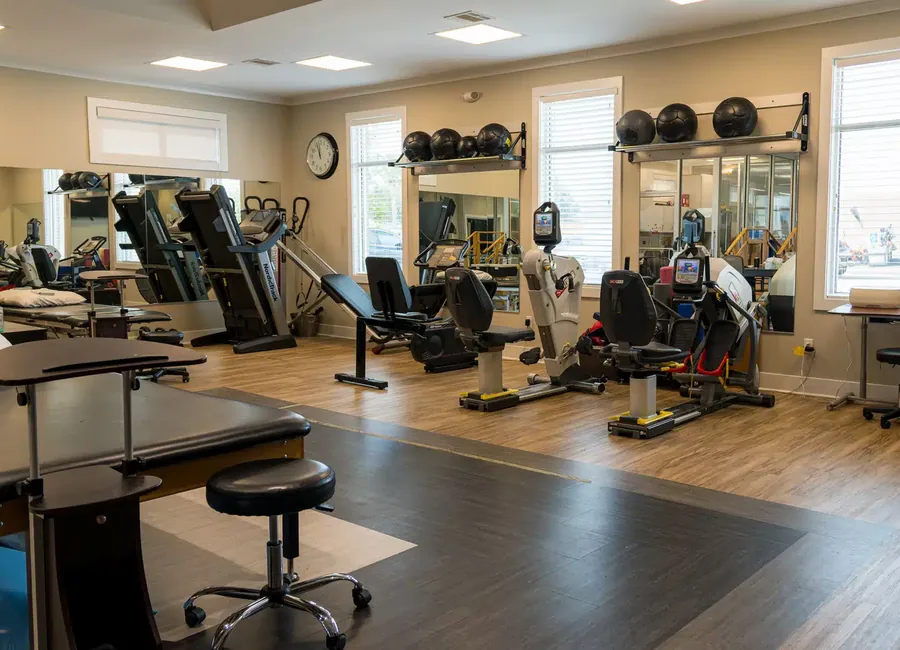 Open physical therapy gym with treatment tables, treadmills, recumbent training machines and wall mirrors