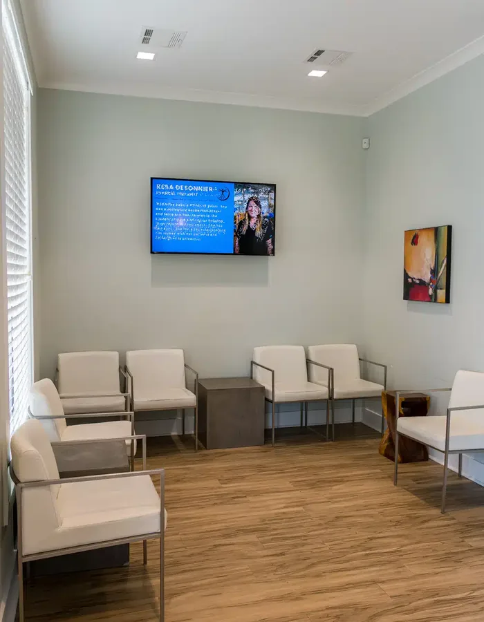 Quiet waiting room with soft green walls, cushioned chairs and a screen introducing the therapy team