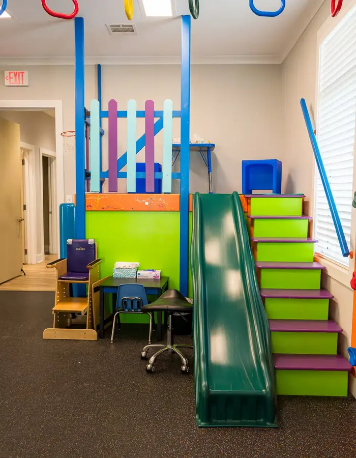 Pediatric treatment area with a green slide, stair platform, adaptive seating and a small work table